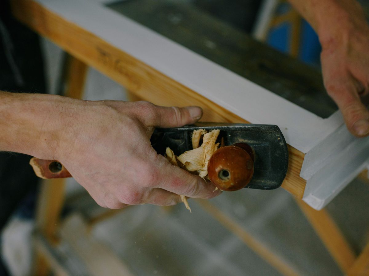 A joiner running a hand plane along a window frame — first-fix carpentry on a renovation